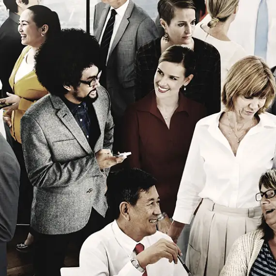 A diverse group of people, likely in a professional or business setting. They appear to be interacting, possibly at a meeting, conference, or a social gathering.