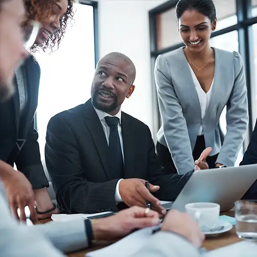 Diverse group collaborates around a laptop in a bright office.